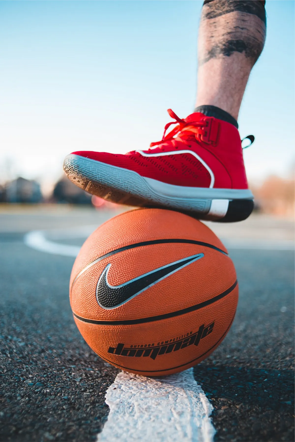Tenis de basquetbol rojo apoyado sobre un balón, en la línea de una cancha al aire libre